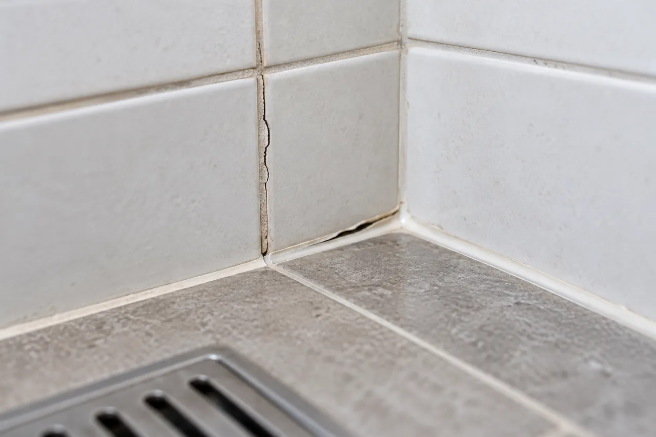 Cracked grout and slightly separated silicone at a tiled shower corner
